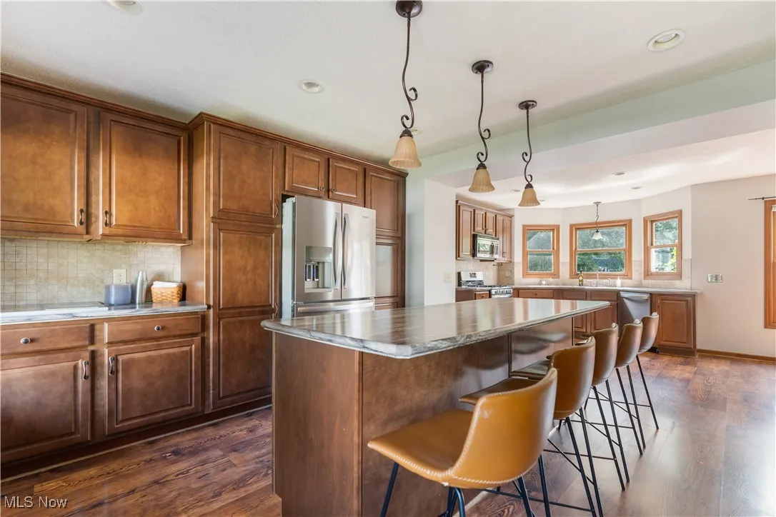 Kitchen featuring backsplash, stainless steel appliances, a breakfast bar, dark wood-style floors, and recessed lighting