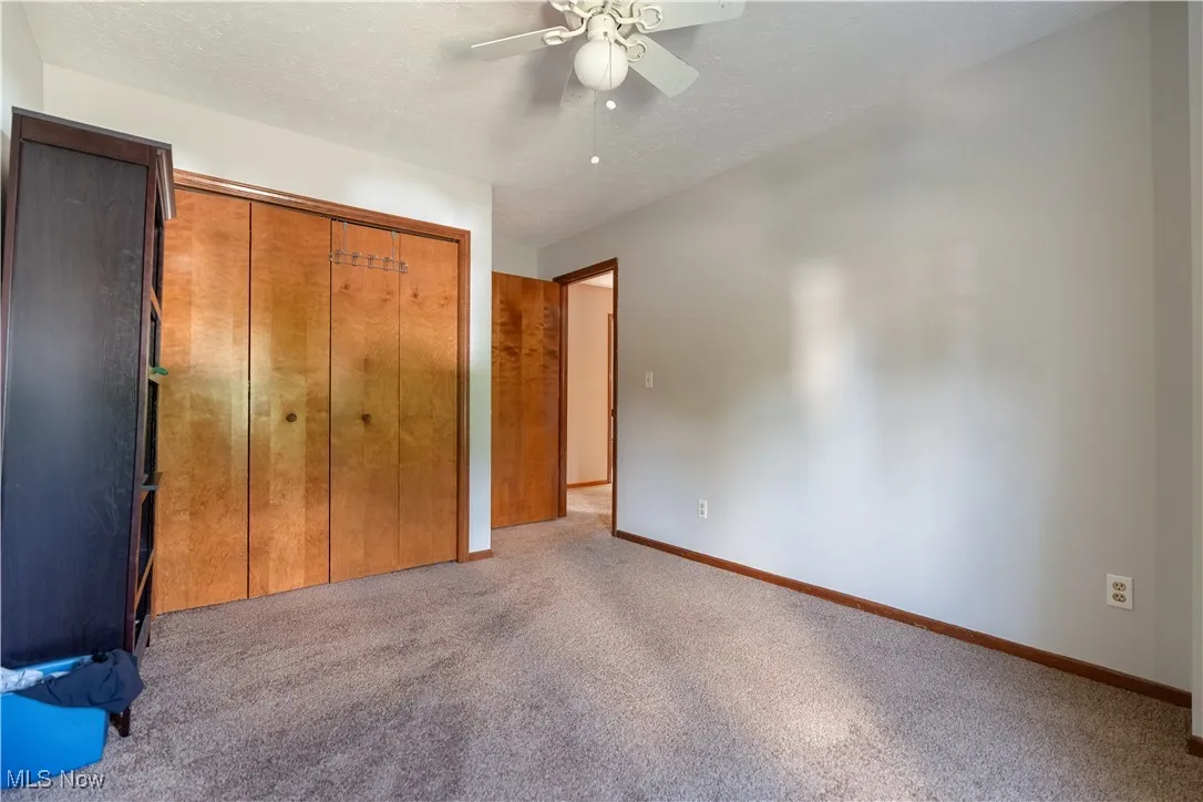 Unfurnished bedroom with a textured ceiling, carpet, a closet, and ceiling fan