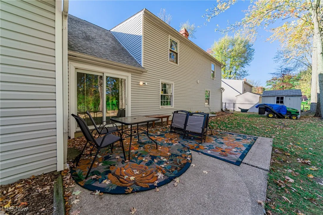 Rear view of property featuring a patio area, a shingled roof, a shed, a chimney, and outdoor dining space