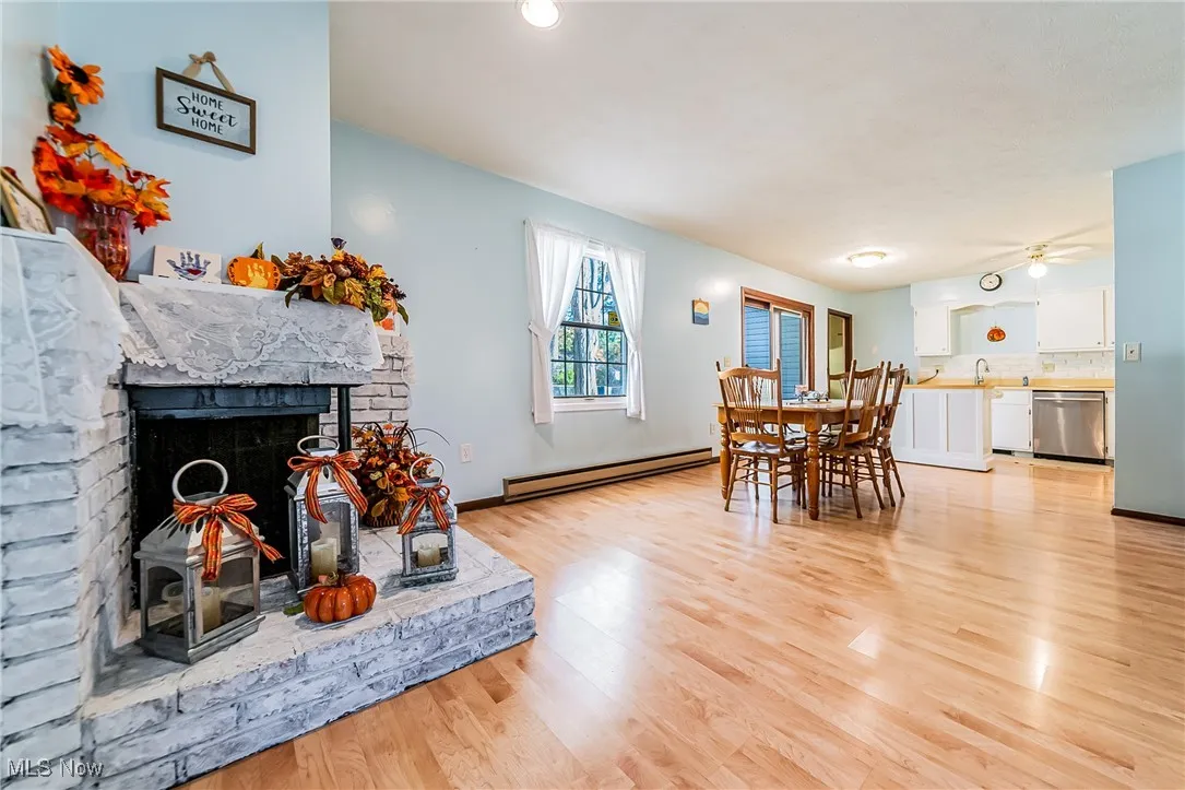 Dining space featuring a fireplace with raised hearth, light wood finished floors, baseboard heating, and a ceiling fan