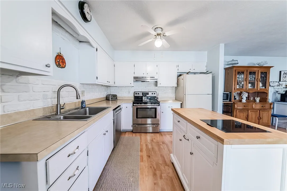 Kitchen with appliances with stainless steel finishes, white cabinetry, decorative backsplash, a kitchen island, and light wood-style flooring