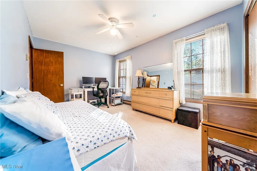 Bedroom with light colored carpet, ceiling fan, and a desk