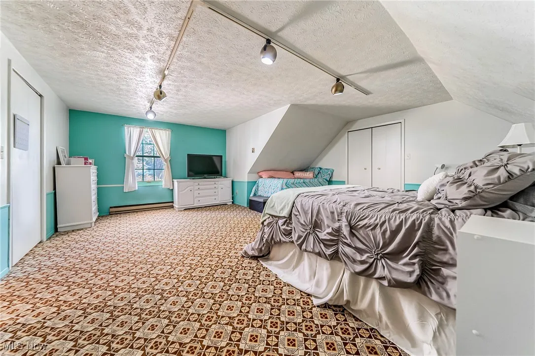 Bedroom with track lighting, a textured ceiling, a closet, baseboard heating, and light colored carpet