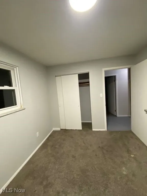 Unfurnished bedroom featuring dark carpet and a closet