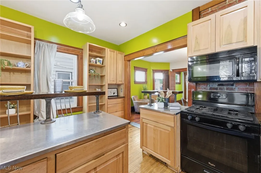 Kitchen with black appliances, light brown cabinets, light wood-style floors, decorative light fixtures, and open shelves