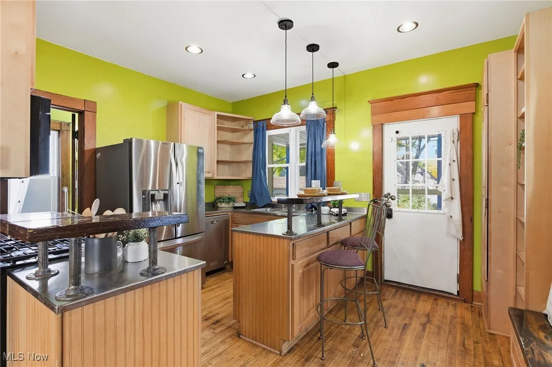 Kitchen featuring open shelves, a peninsula, light wood-style flooring, pendant lighting, and a kitchen breakfast bar