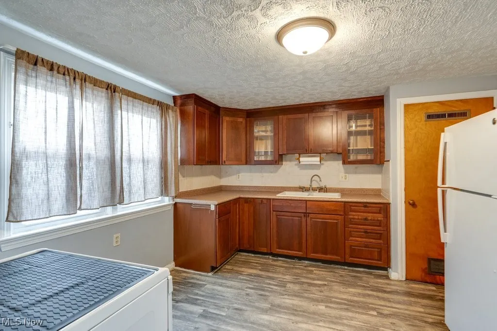 Kitchen with freestanding refrigerator, light countertops, dark wood finished floors, glass insert cabinets, and a textured ceiling