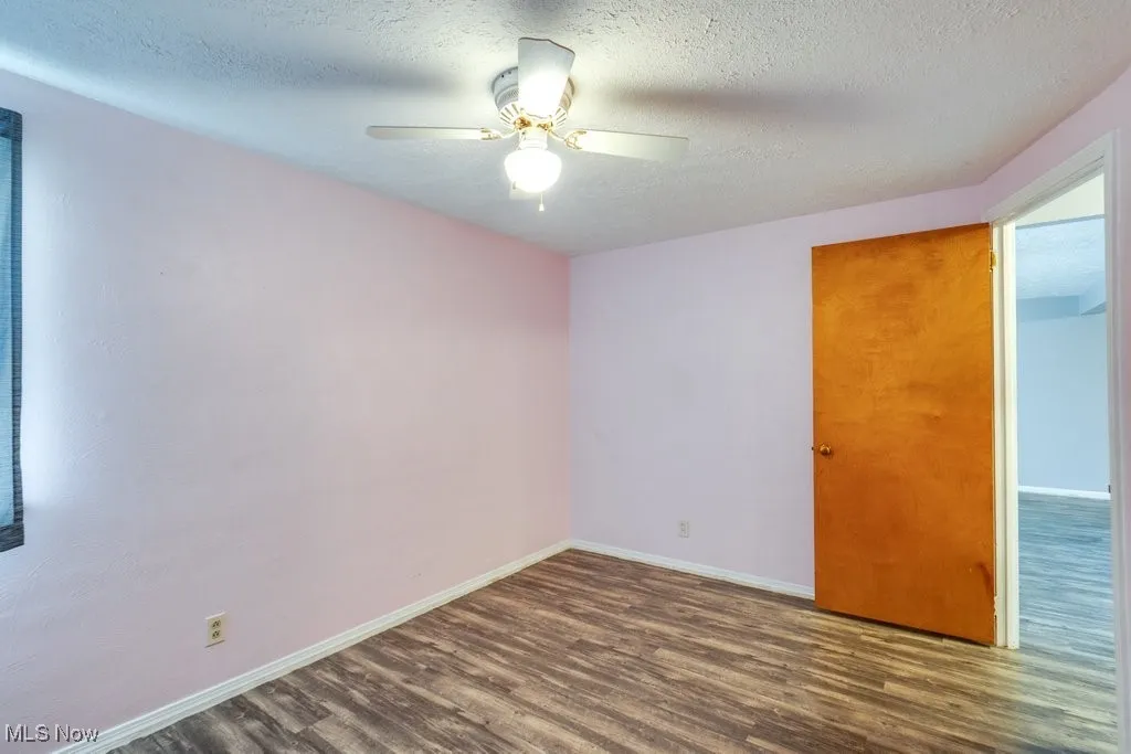 Empty room featuring dark wood-style floors, a textured ceiling, and ceiling fan