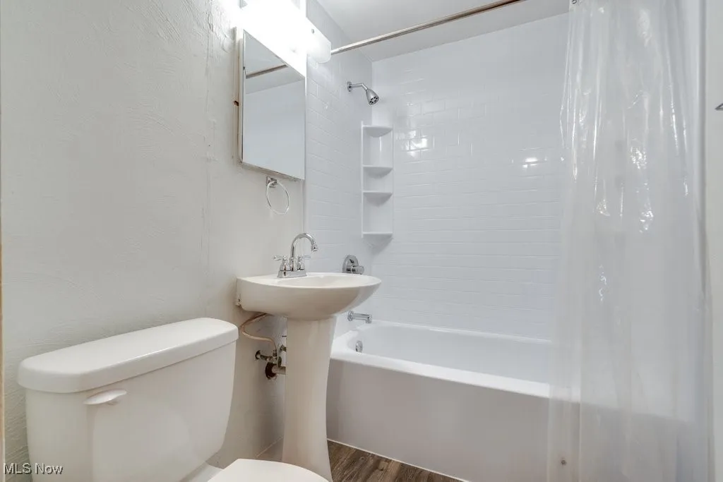 Full bathroom with shower / tub combo with curtain, dark wood finished floors, and a textured wall