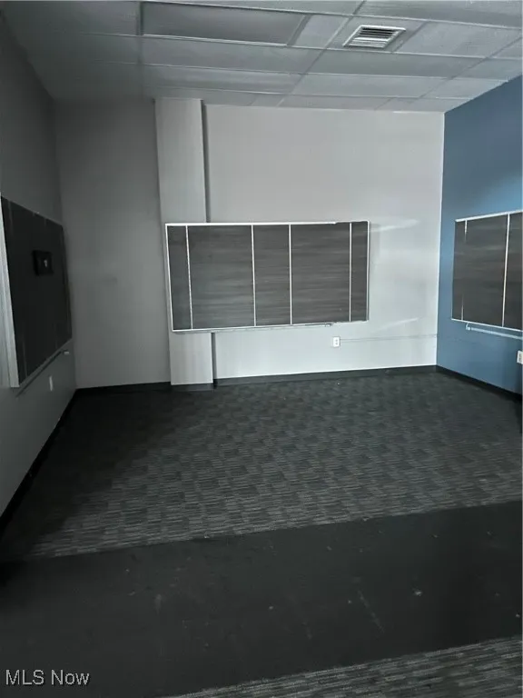 Empty room with dark colored carpet and a paneled ceiling