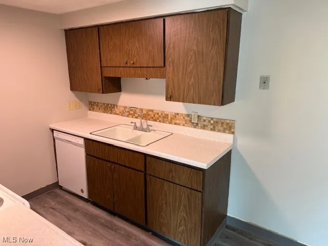 Kitchen featuring light countertops, dishwasher, dark wood-style floors, and decorative backsplash