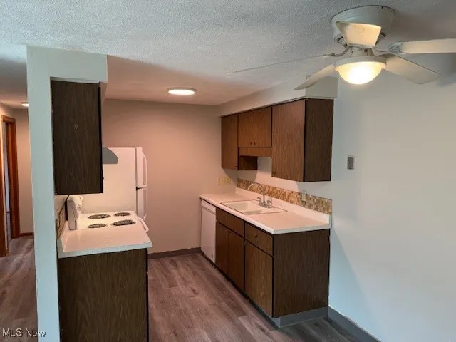 Kitchen featuring dark wood-type flooring, light countertops, white appliances, ceiling fan, and a textured ceiling