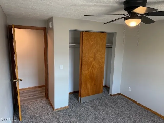 Unfurnished bedroom featuring a textured ceiling, carpet, a closet, and a ceiling fan