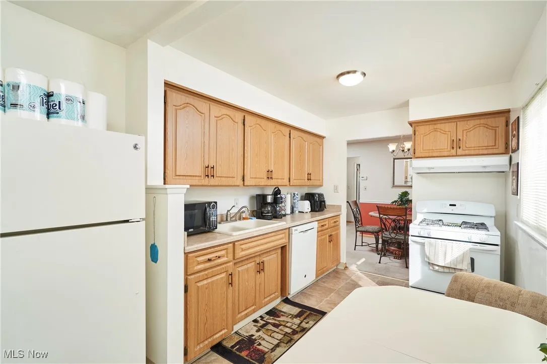 Kitchen with white appliances, light countertops, a chandelier, under cabinet range hood, and light tile patterned floors