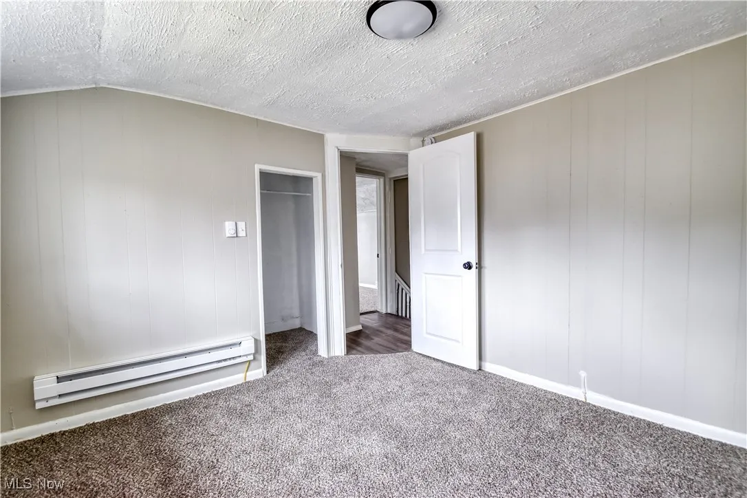 Unfurnished bedroom featuring a baseboard radiator, carpet floors, a textured ceiling, wooden walls, and a closet