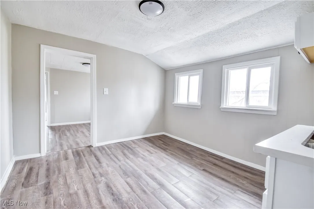Unfurnished room with a textured ceiling, light wood-type flooring, and lofted ceiling