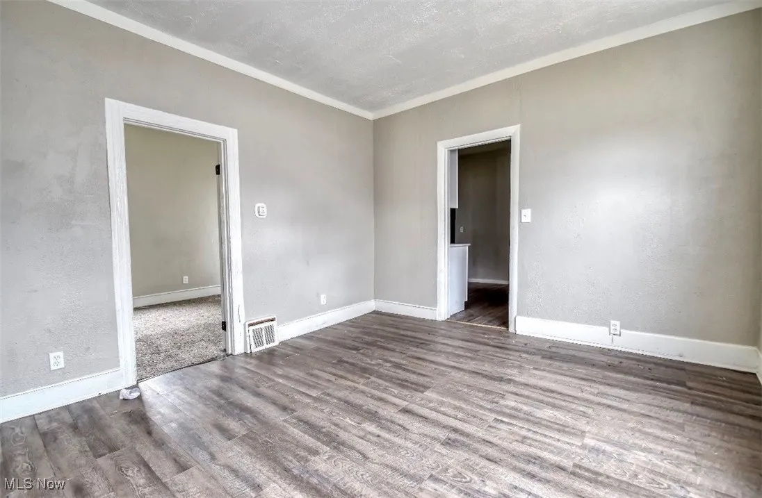 Unfurnished room featuring wood finished floors, a textured wall, a textured ceiling, and ornamental molding
