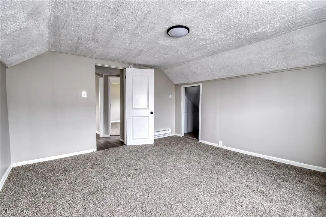 Bonus room featuring a textured ceiling, carpet flooring, vaulted ceiling, and a baseboard radiator