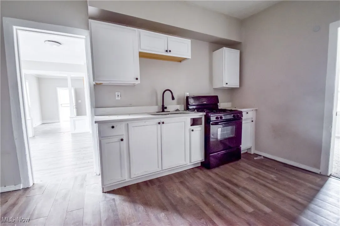 Kitchen featuring black gas stove, white cabinets, light countertops, and dark wood-type flooring