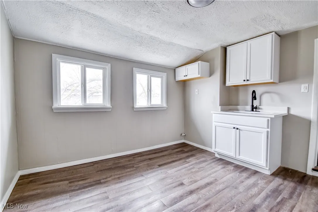 Laundry room featuring a textured ceiling, light wood-type flooring, and lofted ceiling