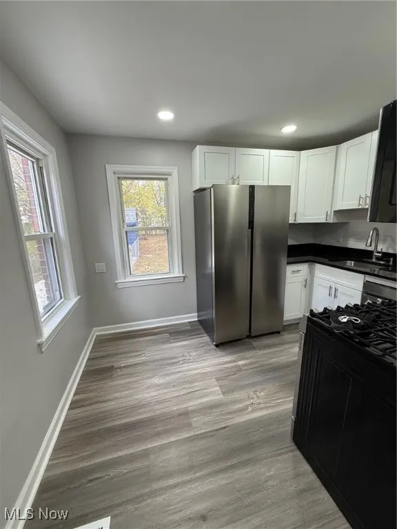 Kitchen featuring stainless steel refrigerator, white cabinetry, light wood-style floors, recessed lighting, and stove