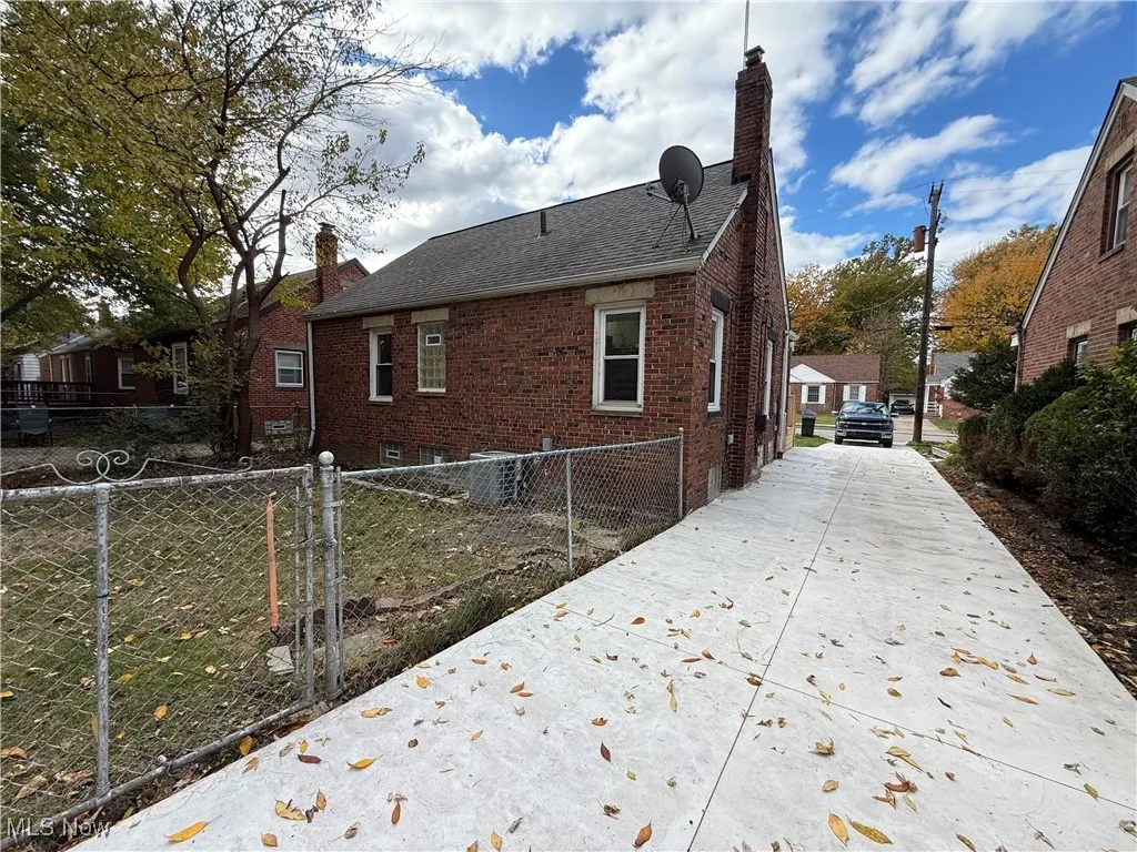 View of side of home with a chimney, brick siding, driveway, and a shingled roof