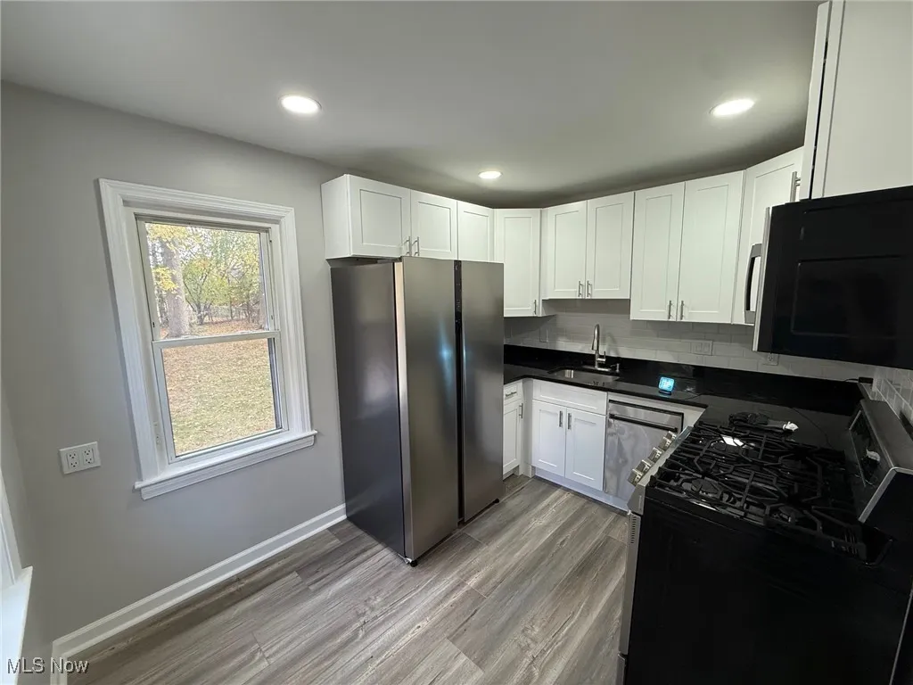 Kitchen featuring black appliances, tasteful backsplash, white cabinetry, wood finished floors, and recessed lighting