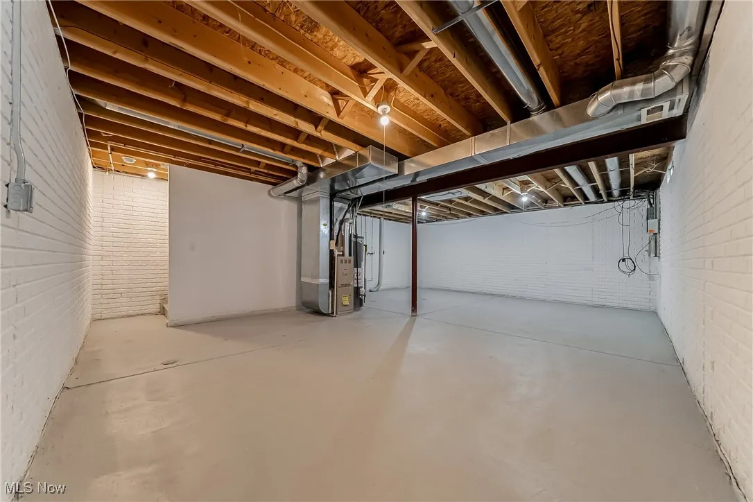 Unfinished basement with brick wall, gas water heater, and heating unit