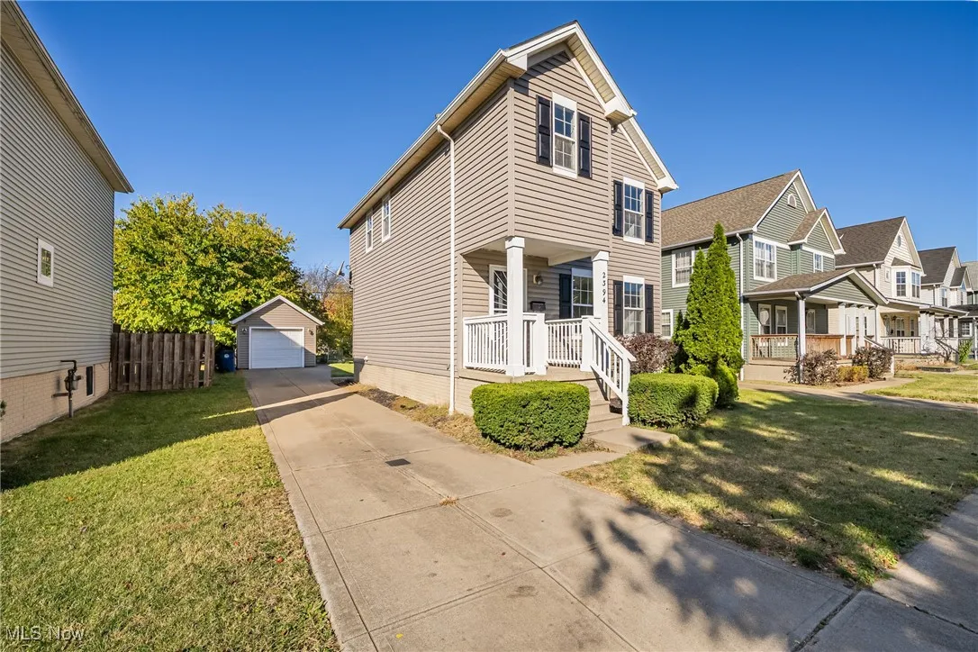 Traditional home with an outbuilding, a detached garage, concrete driveway, a residential view, and covered porch