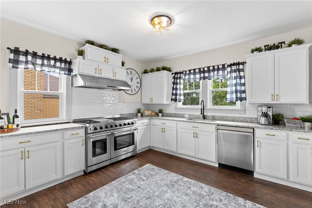Kitchen featuring white cabinets, appliances with stainless steel finishes, light stone countertops, and tasteful backsplash