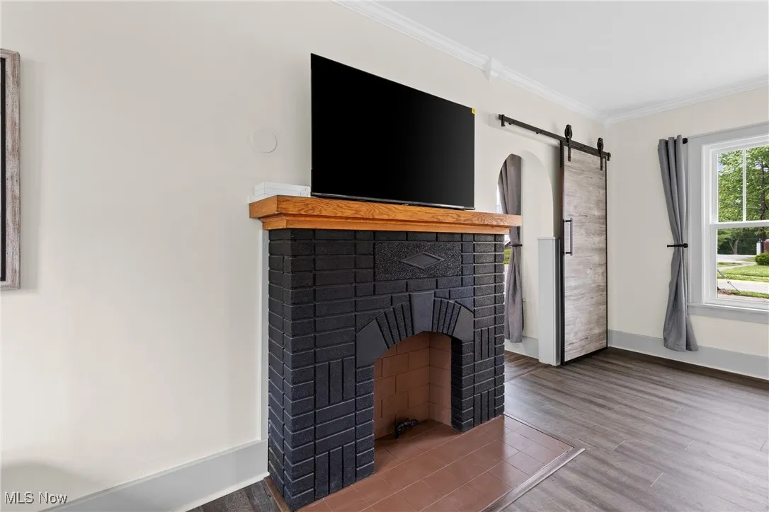 Unfurnished living room featuring a barn door, ornamental molding, wood finished floors, and a fireplace