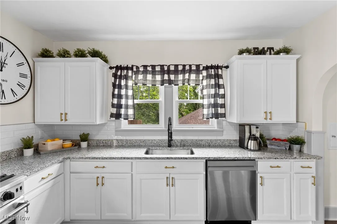 Kitchen featuring stainless steel appliances, white cabinetry, tasteful backsplash, and light stone countertops