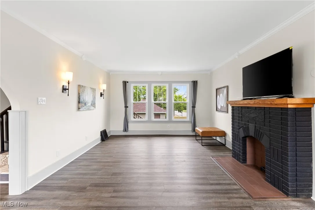 Unfurnished living room with crown molding, wood finished floors, a fireplace, and arched walkways