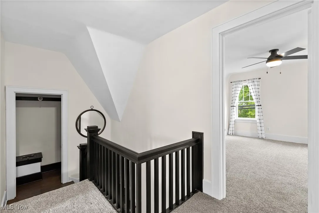 Corridor featuring an upstairs landing, dark colored carpet, and lofted ceiling