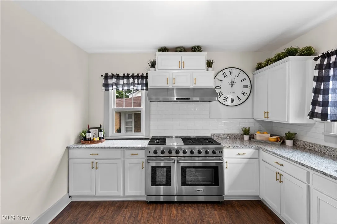 Kitchen featuring white cabinets, range with two ovens, light stone countertops, and dark wood-style floors