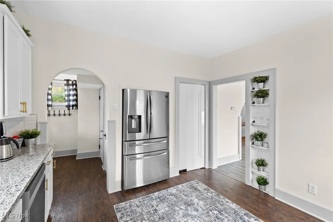 Kitchen featuring stainless steel appliances, white cabinetry, light stone counters, and dark wood-type flooring