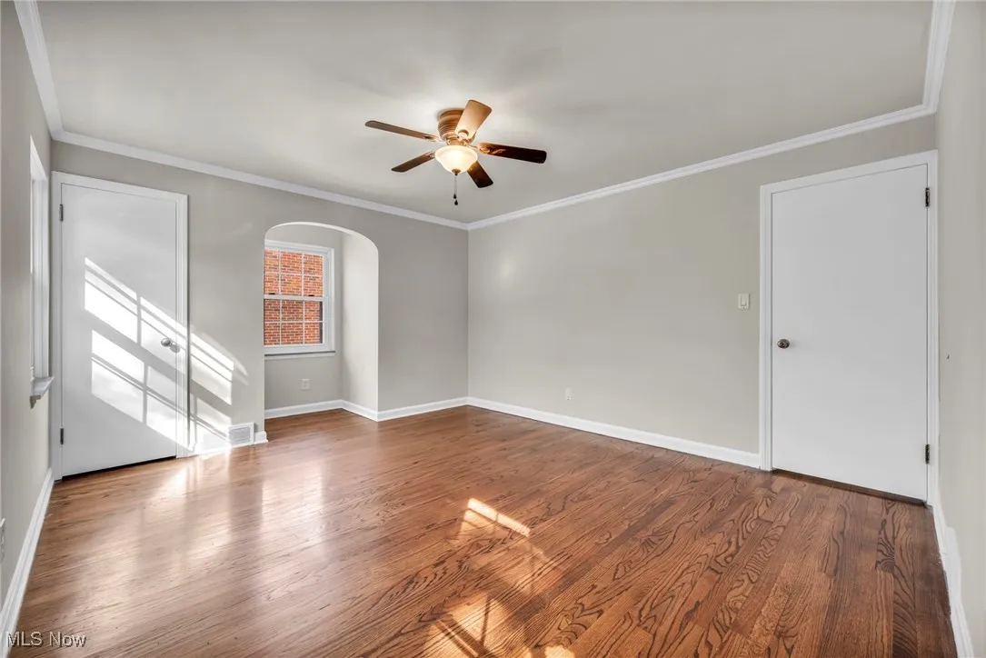 Spare room featuring ornamental molding, arched walkways, wood finished floors, and a ceiling fan