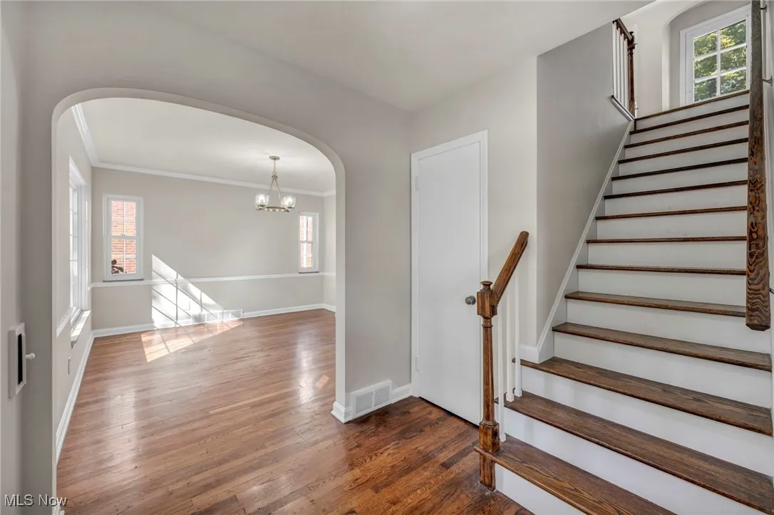 Stairway featuring wood finished floors, ornamental molding, arched walkways, and a chandelier