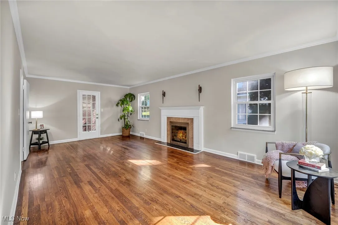 Living room featuring ornamental molding, wood finished floors, and a fireplace with flush hearth