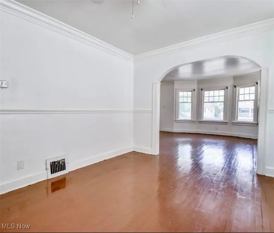 Unfurnished room with arched walkways, ornamental molding, and dark wood-style flooring