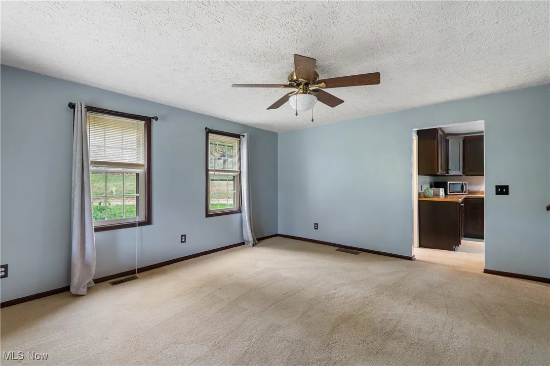 Empty room with light colored carpet, a textured ceiling, and ceiling fan