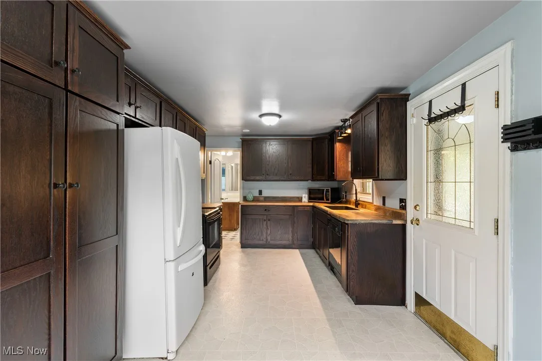 Kitchen with dark brown cabinets, black appliances, and light countertops