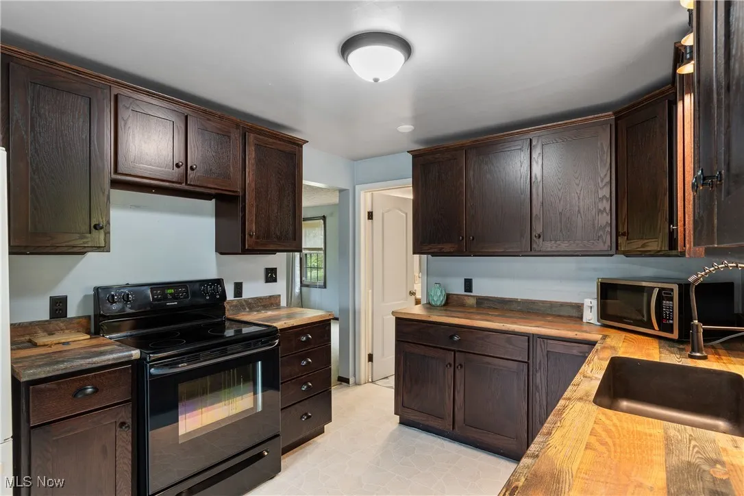 Kitchen featuring black electric range, dark brown cabinetry, butcher block countertops, and stainless steel microwave
