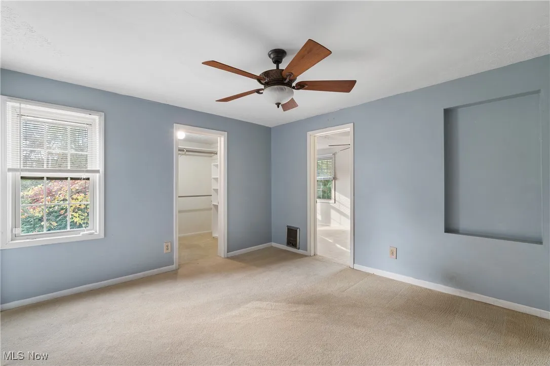 Unfurnished room featuring a walk in closet, carpet, and a ceiling fan