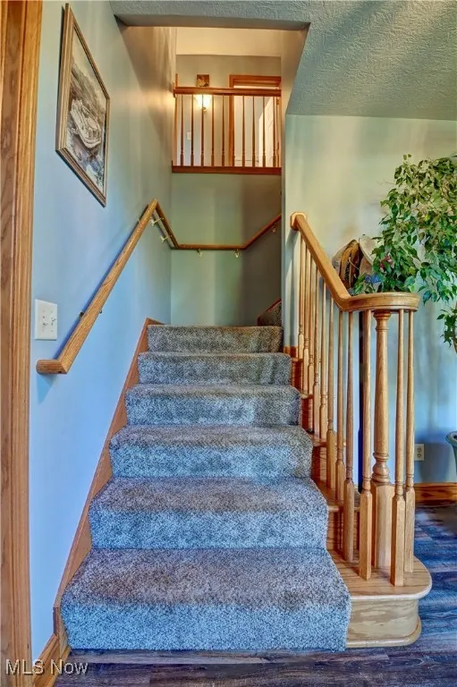 Stairway with a textured ceiling and wood finished floors