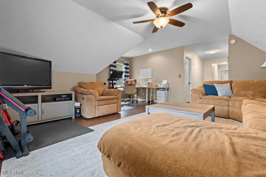 Bedroom with wood finished floors, vaulted ceiling, ceiling fan, a textured ceiling, and a desk