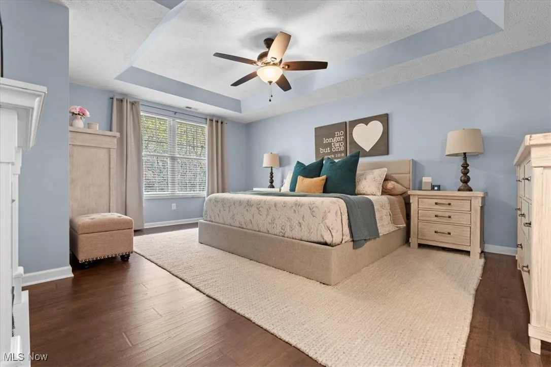 Bedroom featuring a tray ceiling, dark wood-type flooring, a ceiling fan, and a textured ceiling
