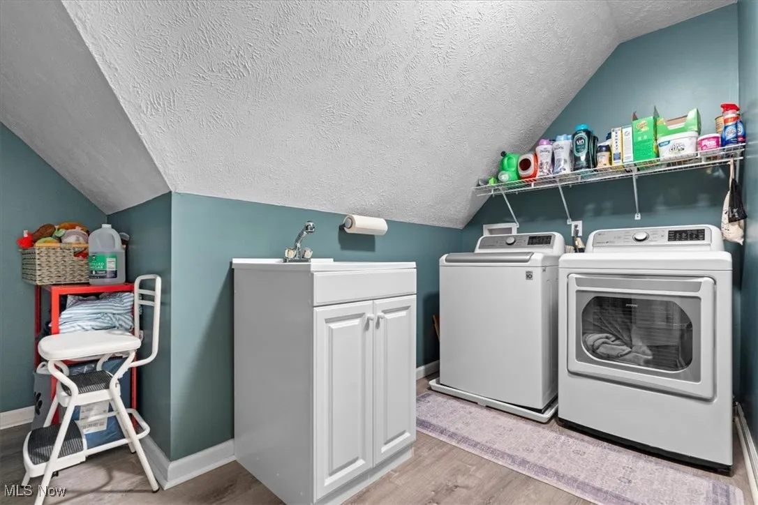 Washroom featuring a textured ceiling, vaulted ceiling, light wood finished floors, and washing machine and clothes dryer