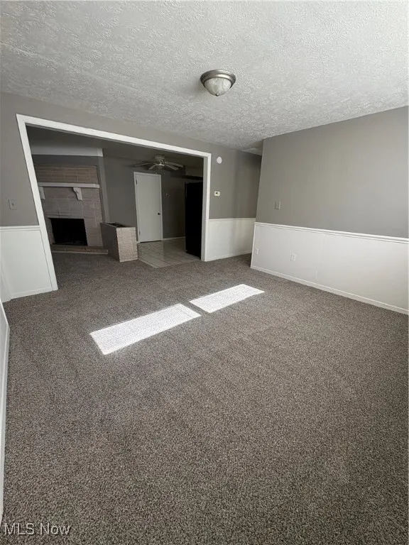 Unfurnished bedroom with a fireplace with raised hearth, carpet floors, a textured ceiling, a closet, and a wainscoted wall