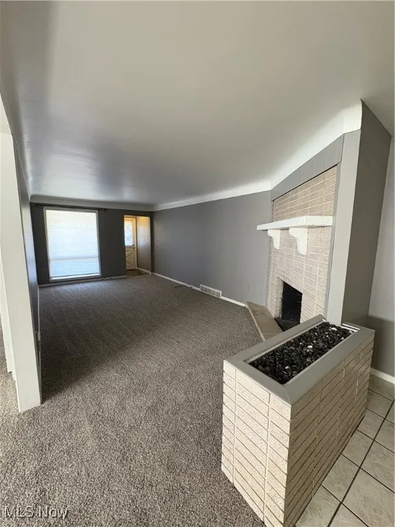 Unfurnished living room with a brick fireplace and light colored carpet